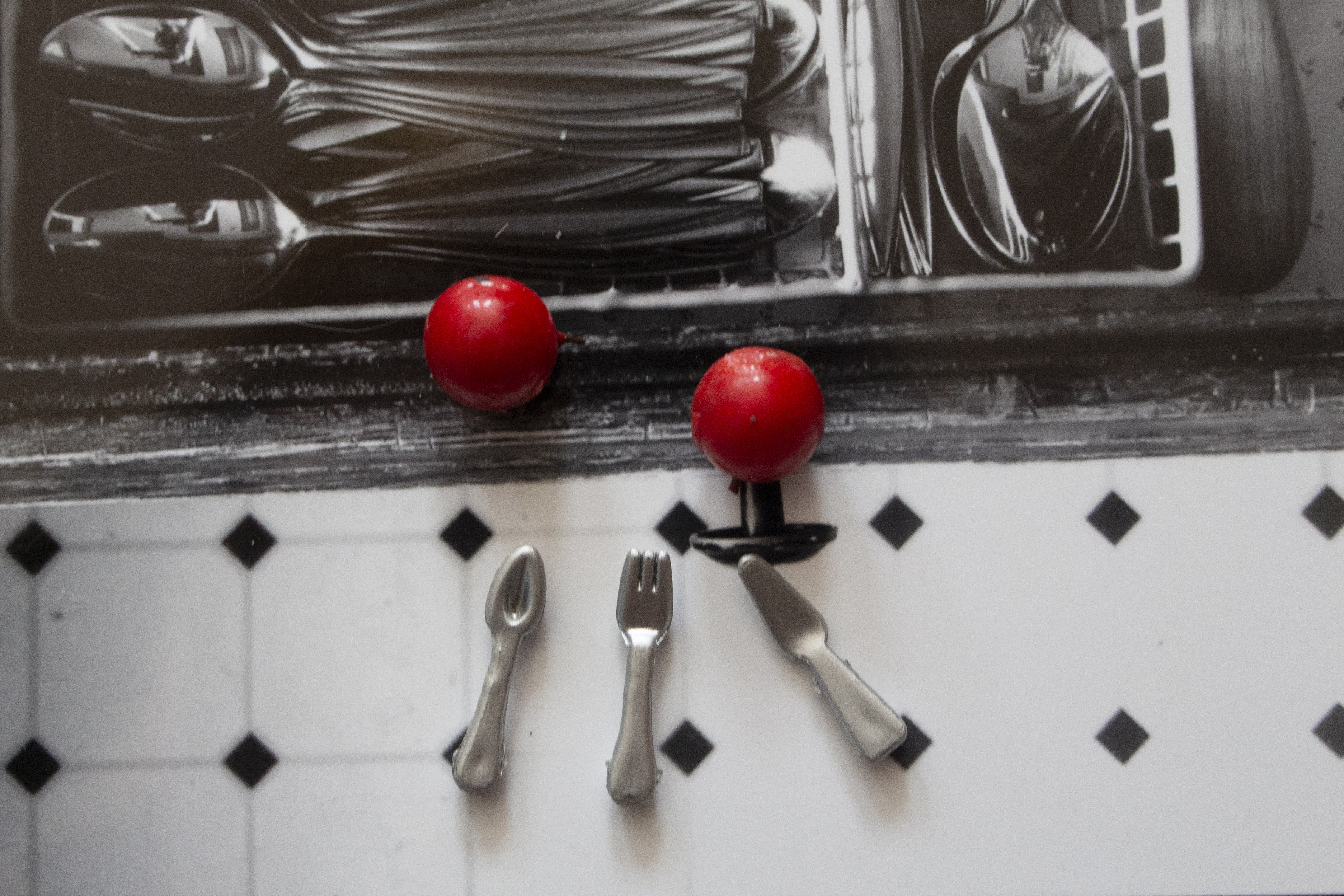 Miniature silverwear and apples float above a background of a halfway open silverwear drawer and a tiled linoleum floor
