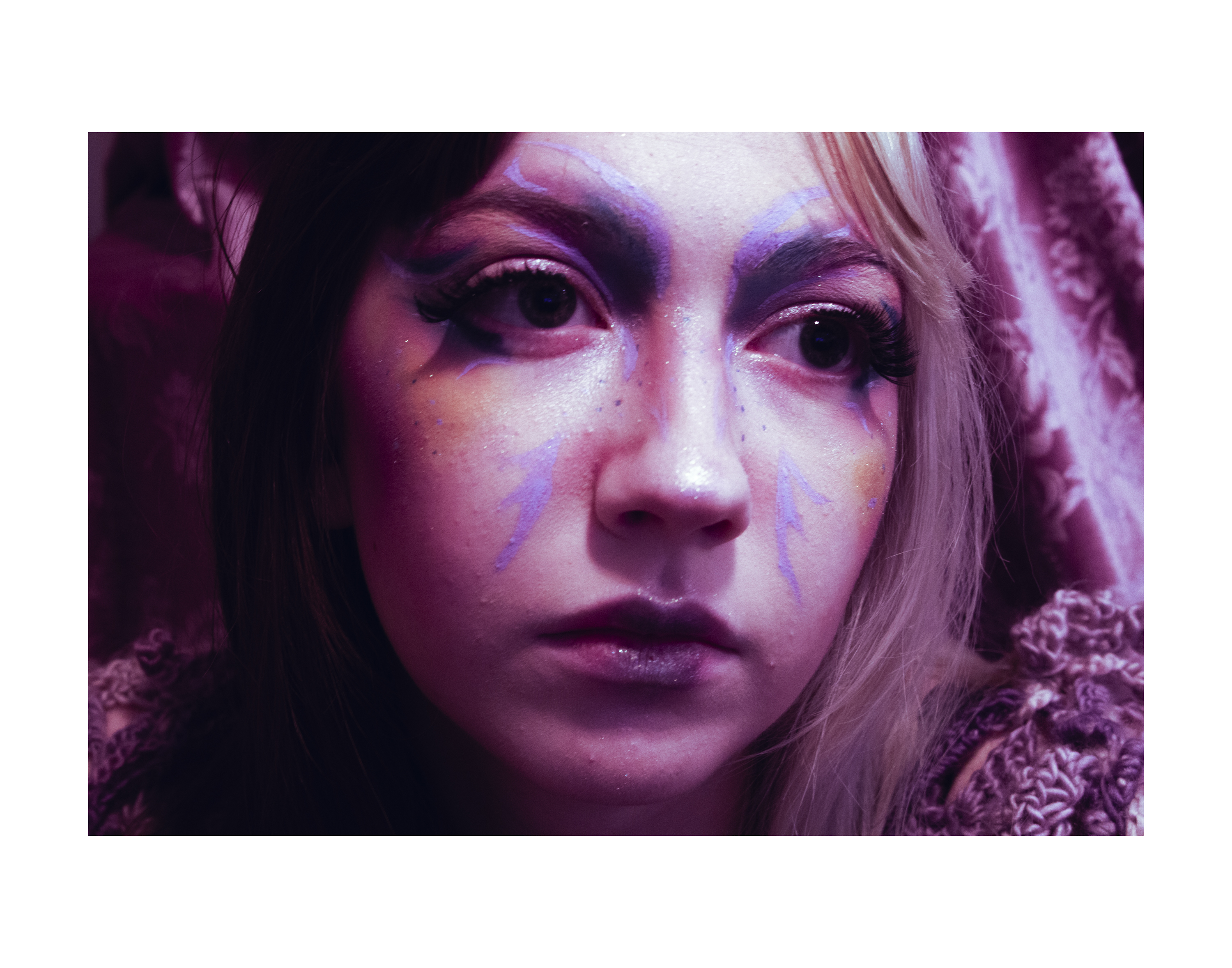 Image of a purple-toned woman's face with various almost imperceptable lines drawn on her face, like the wings of a butterfly