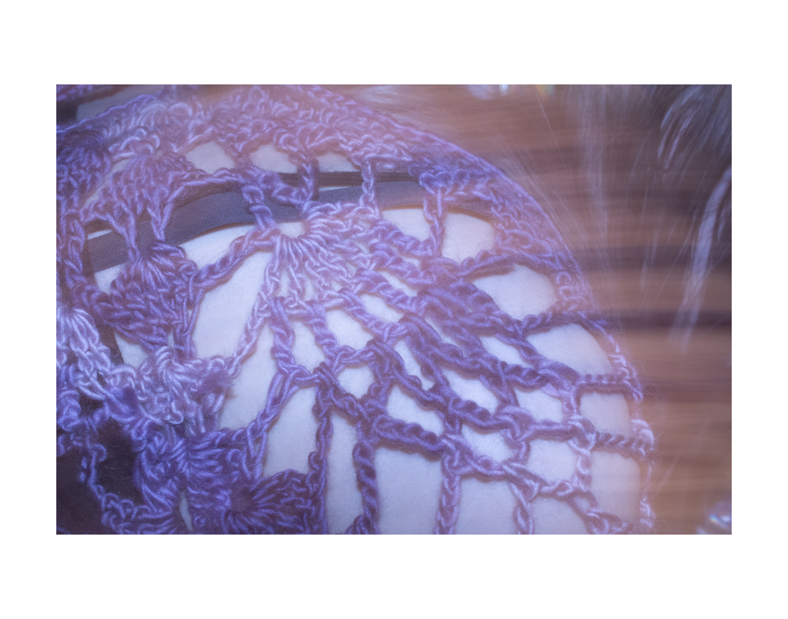 An image of a woman's shoulder, shrouded beneath a complex web of purple crocheted yarn