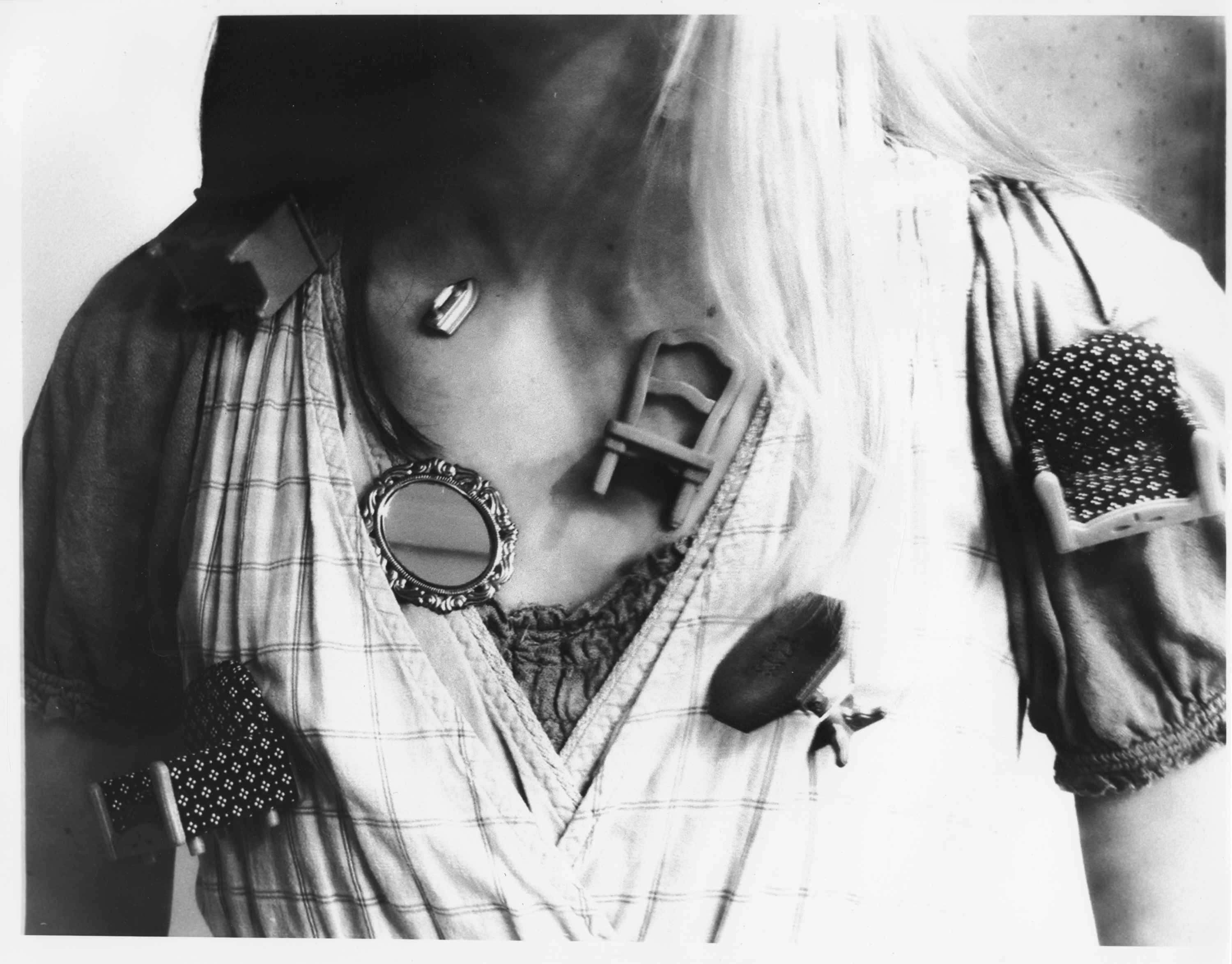 Black and white photograph of a woman's torso with various dollhouse furnitures sticking to her skin and clothing